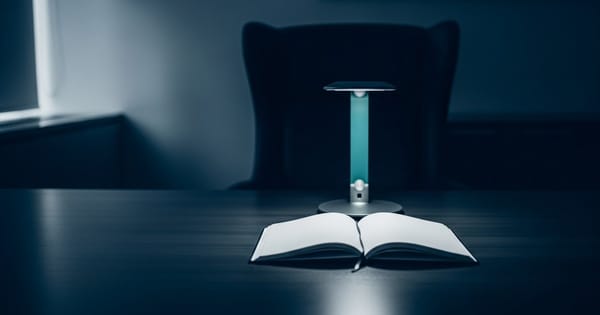 A single illuminated desk lamp over an open blank notebook in a dark office