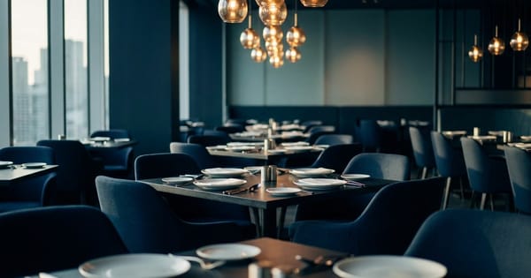 An elegant empty restaurant interior at golden hour with set tables and warm pendant lighting